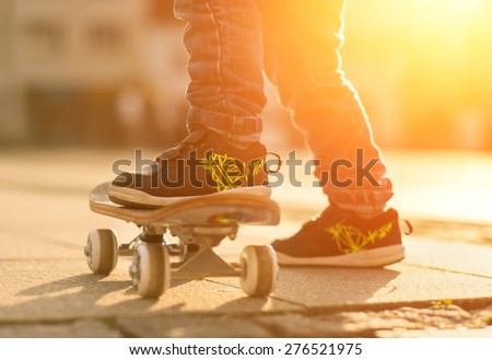 Child with skateboard on the street at sunset light.