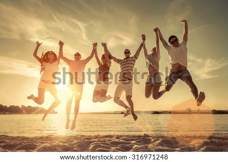 Friends jumping on the beach under sunset sunlight.