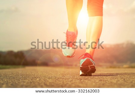 Runner athlete feet running on road under sunlight.
