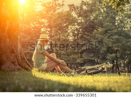 Woman sitting under sun light at day near her bicycle in the park