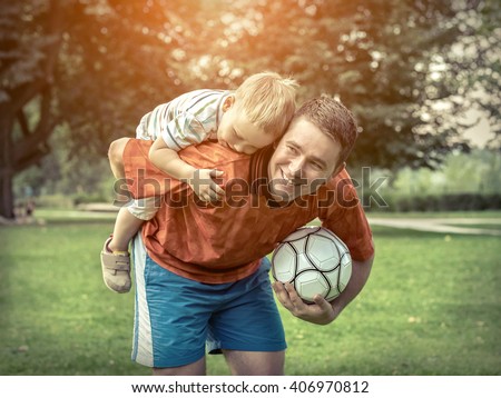 Father and son playing football in park at sunny day