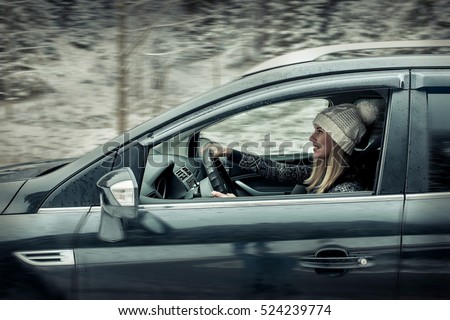 Woman at winter time. Yoyng female sitting and driving in black car at snowly winter day.