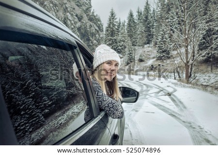 Woman at winter time. Yoyng female looking in window of her black car at snowly winter day.