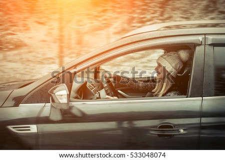 Woman at winter time. Yoyng female sitting and driving in black car at snowly winter day.
