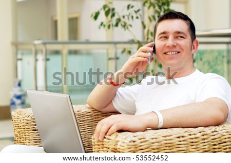 Smiling young man working on laptop computer and call by phone at home