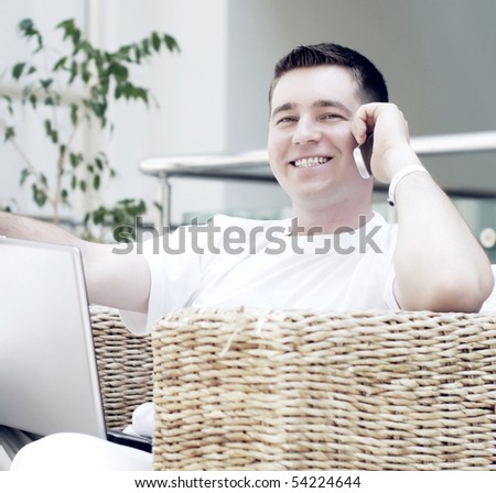 Smiling young man working on laptop computer and call by phone at home