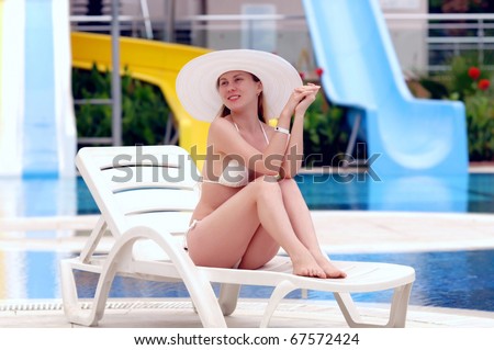 Young women in white bikini and white hat relaxing near waterpool