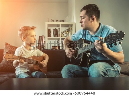 Father teaching his son to play on guitar at home. Son play on ukulele - hawaiian guitar.