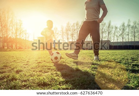 Father and son playing together with ball in football under sun light. Green field in city park at sunny day.