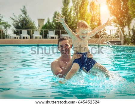 Father and son funning in water pool under sun light on summer day. Leisure and swimming at holidays.