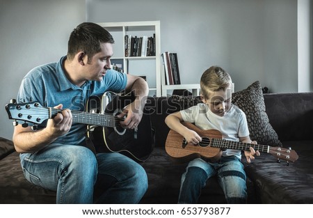 Father teaching his son to play on guitar at home. Son play on ukulele - hawaiian guitar.