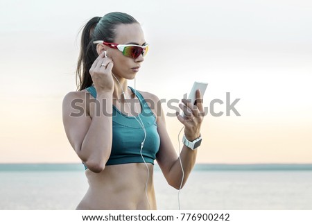 Running woman in sport sunglasses. Female runner with her smartphone training outdoor workout on beach. Beautiful fit mixed race Fitness model outdoors.