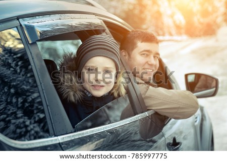 Happiness caucasian smilling boy with his father looking out of black car window in sunny day at winter time near the forest.