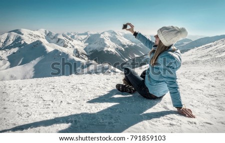 Happy woman relaxing on the top of mountain under blue sky with her camera at sunny winter day, travel vacation, landscape mountains background.