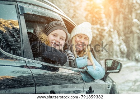 Happiness caucasian smilling boy with his mother looking out of black car window in sunny day at winter time near the forest.