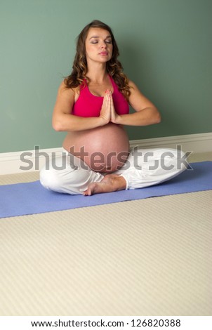Prenatal Yoga - Pregnant woman sitting in a lotus position while meditating.