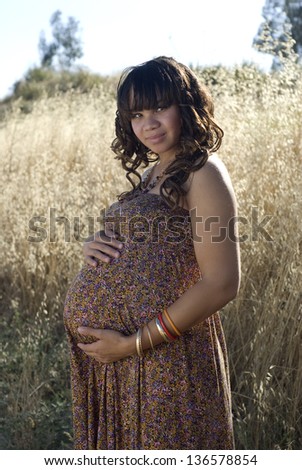 Posing pregnancy - Young mother-to-be posing in a field of tall grass.