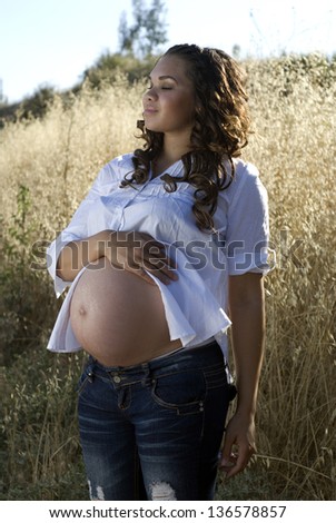 Pregnancy hope - Young mother-to-be posing in a field of tall grass.