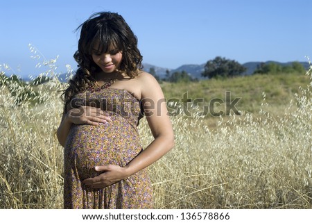 Joyful pregnancy - Young mother-to-be posing in a field of tall grass.