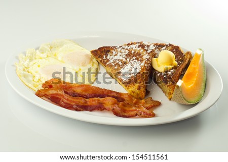 French toast breakfast plate - French toast with powdered sugar and butter on a plate with bacon, eggs and cantaloupe. White background.