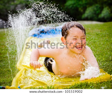 Happy child on water slide to cool off on hot day during spring or summer