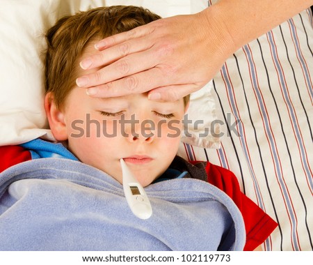Sick child boy being checked for fever and illness while resting in bed