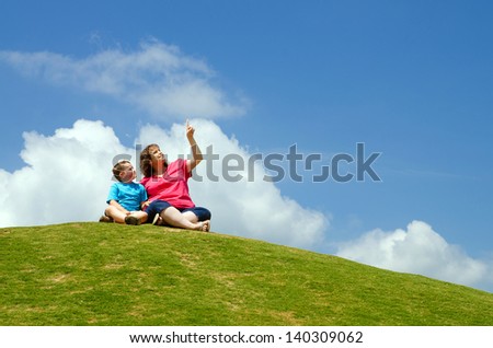 Mother and son watching clouds from grassy hill