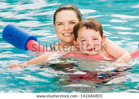 Mother giving son a swimming lesson in pool during summer