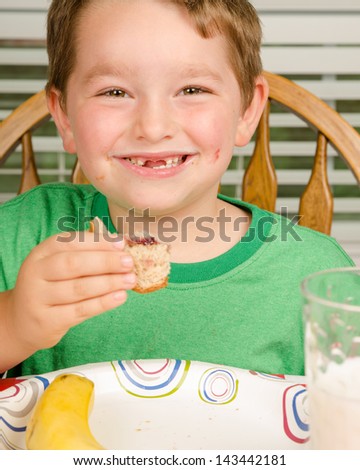 Child eating messy peanut butter and jelly sandwich with milk and fruit for healthy lunch