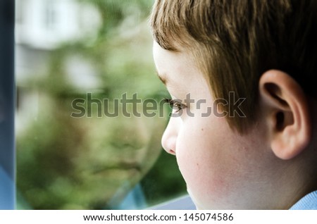 Sad child looking out window with reflection on gloomy day