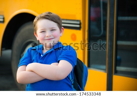 Happy young boy in front of school bus going back to school