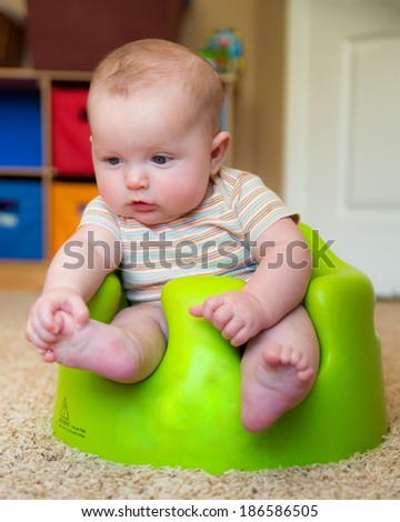 Infant baby boy discovering and playing with this feet while using training Bumbo seat to sit up