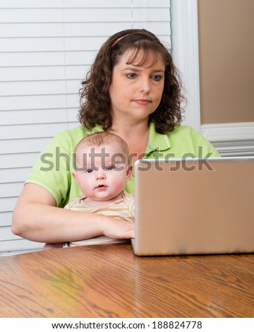 Mother holding baby while working on her computer