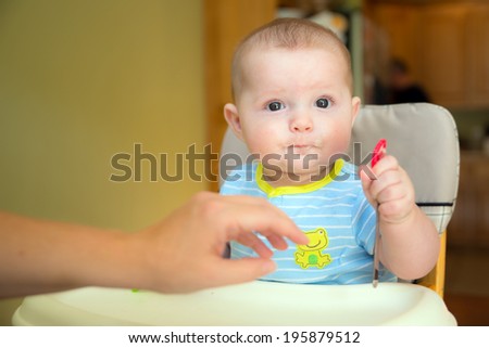 Happy baby infant boy eating meal while sitting in high chair