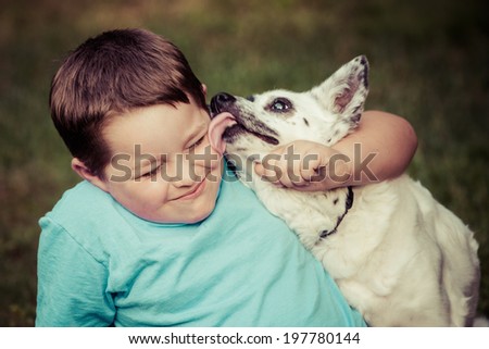 Happy boy being licked by his pet dog in image with vintage filter