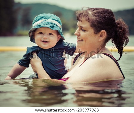 Mother teaching infant baby son to swim in lake during summer in vintage filtered image