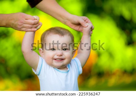 Smiling happy baby learning to walk outdoors
