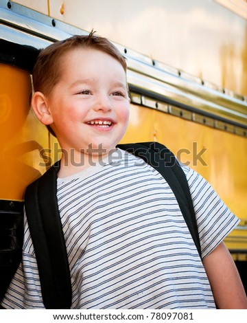 Happy young boy in front of yellow school bus waiting to board on first day back to school.