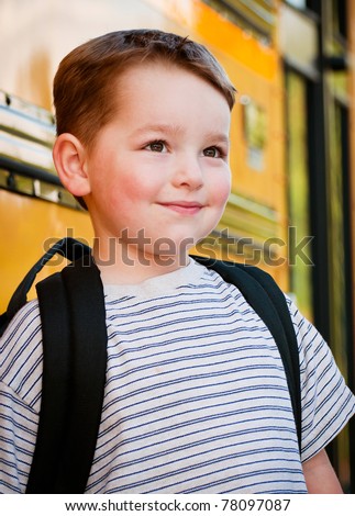 Content young boy in front of yellow school bus waiting to board on first day back to school.
