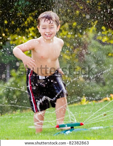 Young boy or kid cools off by playing in water sprinkler at home in his back yard on hot summer day