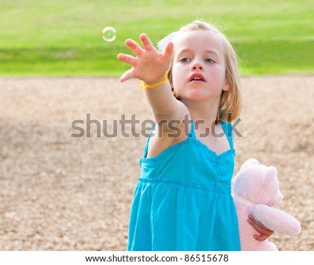 Young girl trying to catch bubble while playing at park in image with copy space