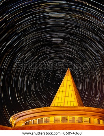 Circles of star trails behind roof of modern building