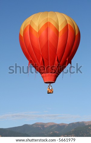 One colorful hot air balloon with the Rocky Mountains as backdrop during an early morning ascend