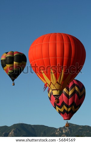 Three colorful hot air balloons during an early morning ascend with the Rocky Mountains as backdrop