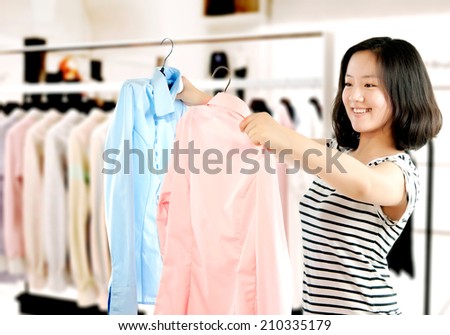 Woman shopping buying new dress in clothing shop choosing between two dresses.