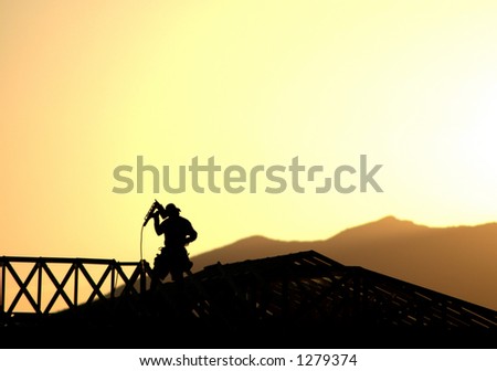Construction worker framing a new home silhouetted against the evening sunset and mountains.