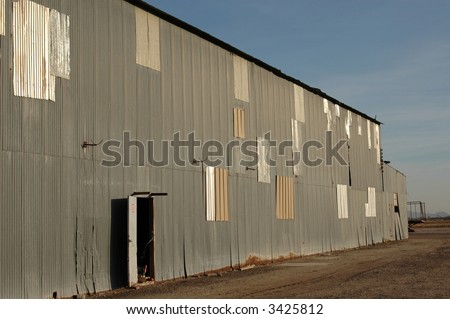 Abandoned agricultural warehouse with open side door. Past repair work can be clearly seen.