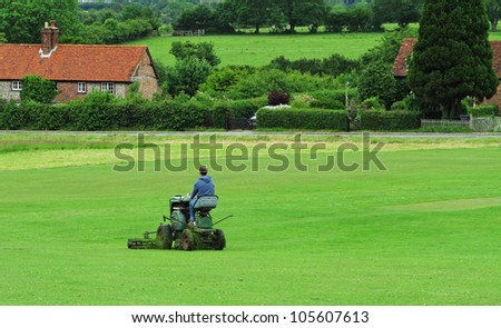 Man cutting the grass on an English Village Cricket Field