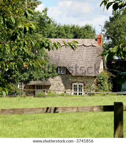 Thatched  English Rural Cottage with fence and Field in front