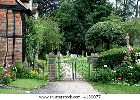 Wrought Iron Entrance Gate to an English Village Churchyard with flowers and Timber Framed Cottage